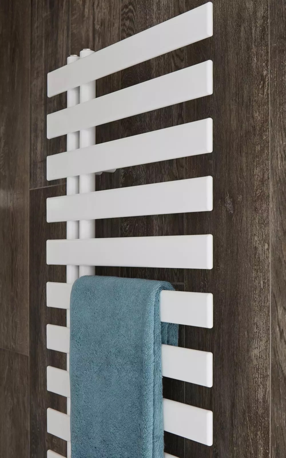 Badheizköper Cha-cha von Bemm an einer Holzoptik-Wand, mit einem blauen Handtuch darüber.