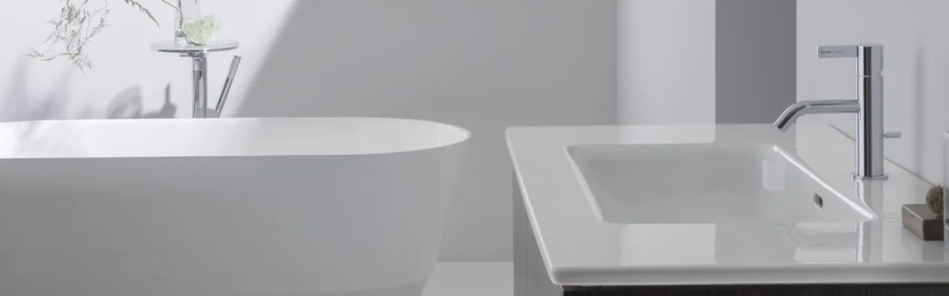 Ein modernes Badezimmer mit einer freistehenden weißen Badewanne auf der linken Seite und einem weißen Waschbecken mit einer Chromarmatur rechts.