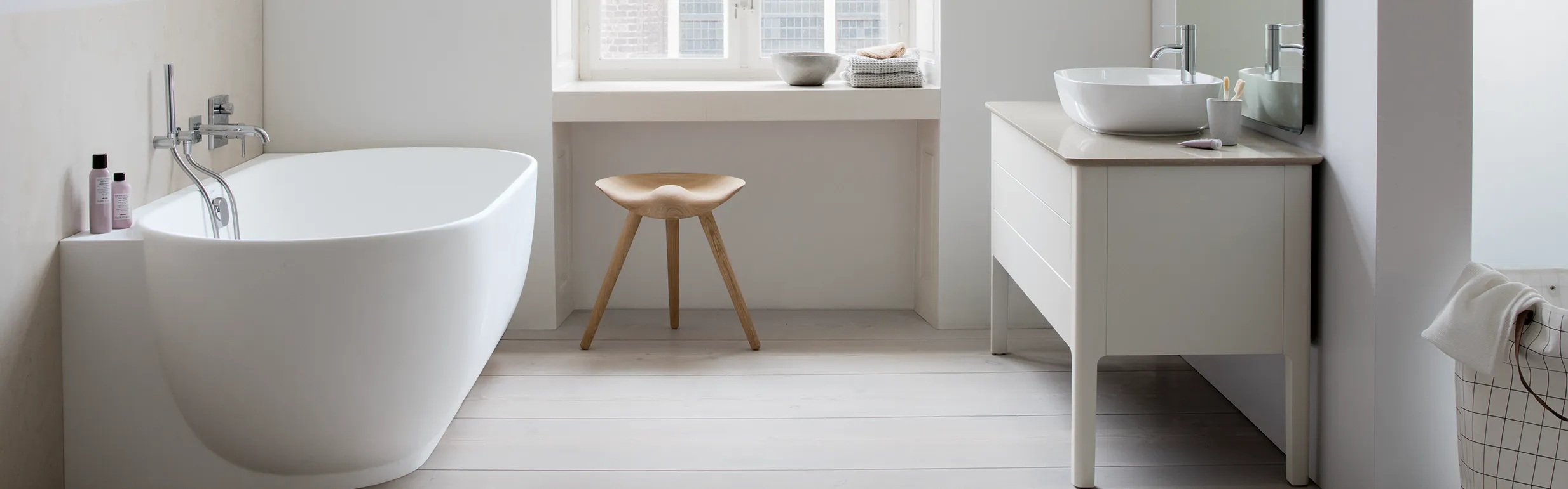 Ein minimalistisches Badezimmer mit einer freistehenden weißen Badewanne und einer modernen Armatur an der Wand.