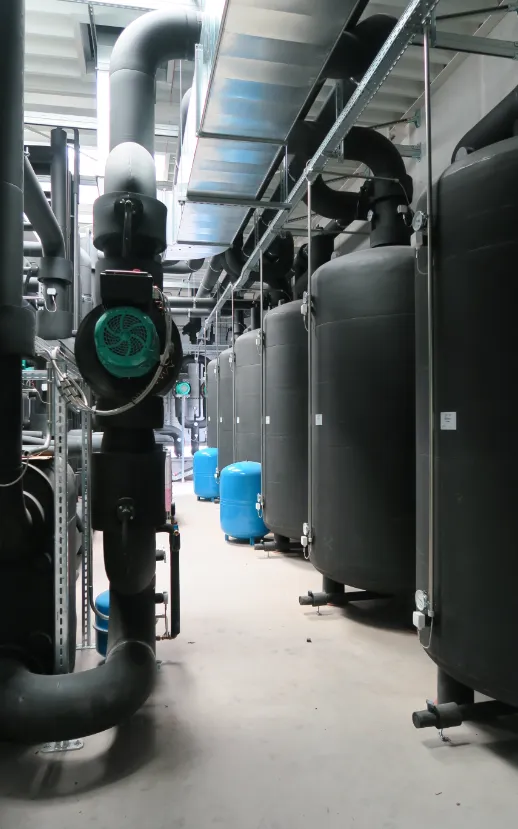 Technikraum mit großen schwarzen Pufferspeichern, Rohrleitungen und Pumpenanlagen zur Wärme- und Energieversorgung.
