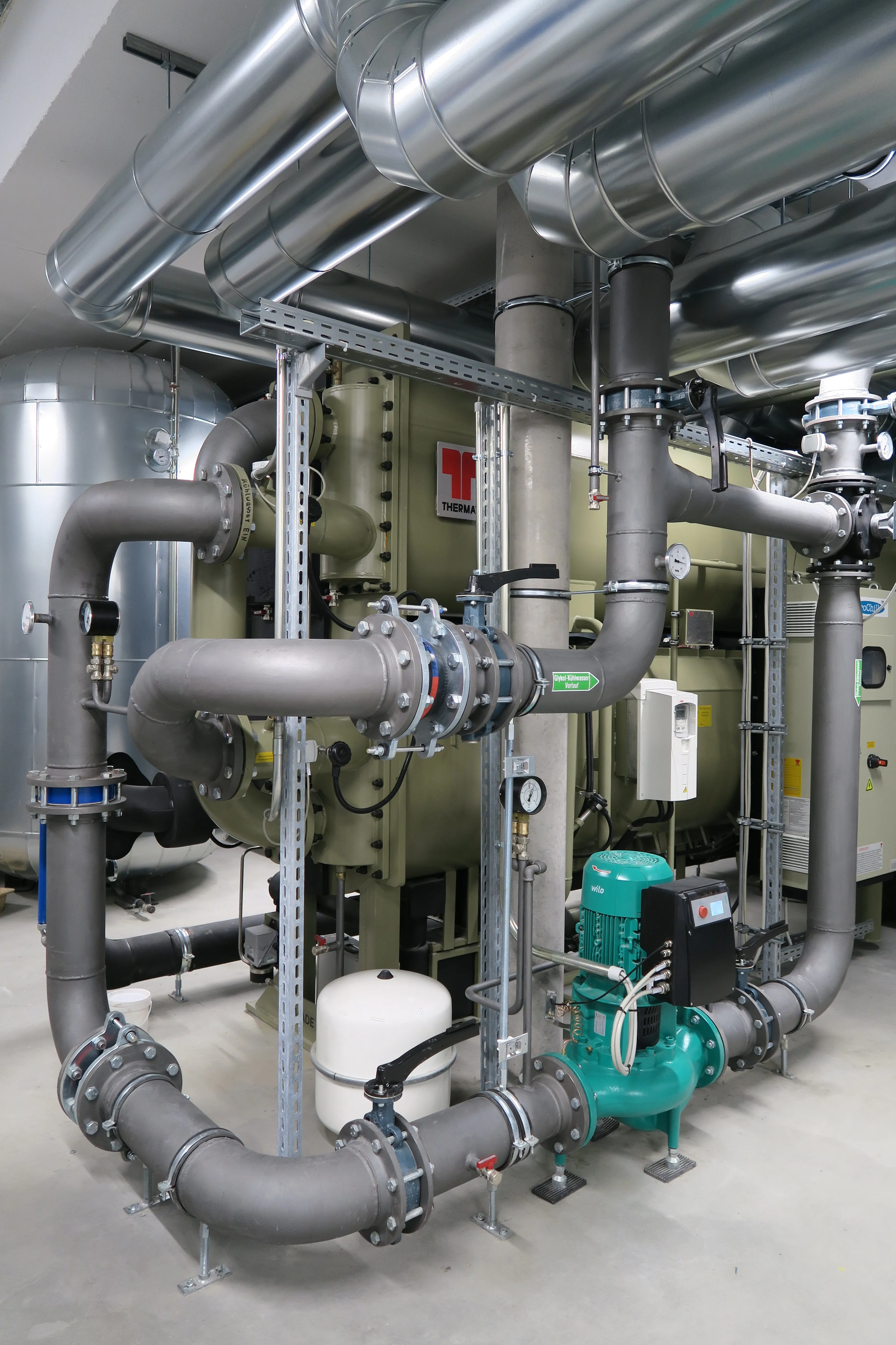 Technikraum mit industrieller Kälteanlage, großen Rohrleitungen, Umwälzpumpe und Wärmetauscher der Marke Thermax.