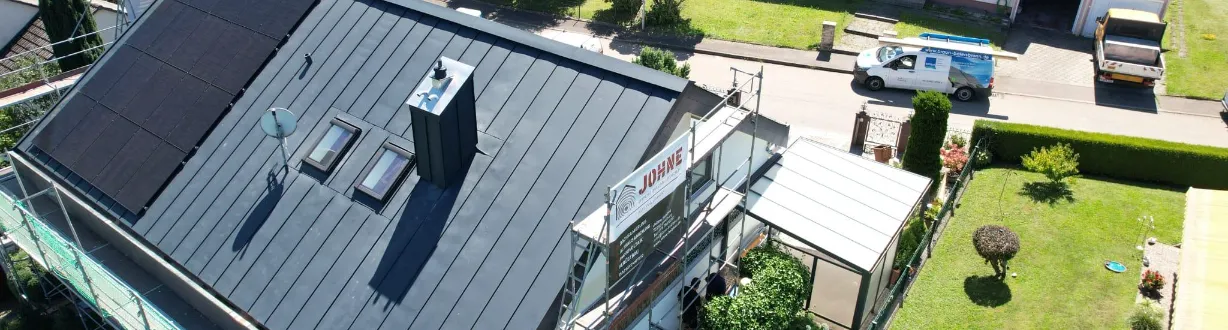 Luftaufnahme eines Wohngebäudes mit neuem, dunkel gedecktem Schrägdach und großflächiger Photovoltaikanlage auf der linken Dachseite.