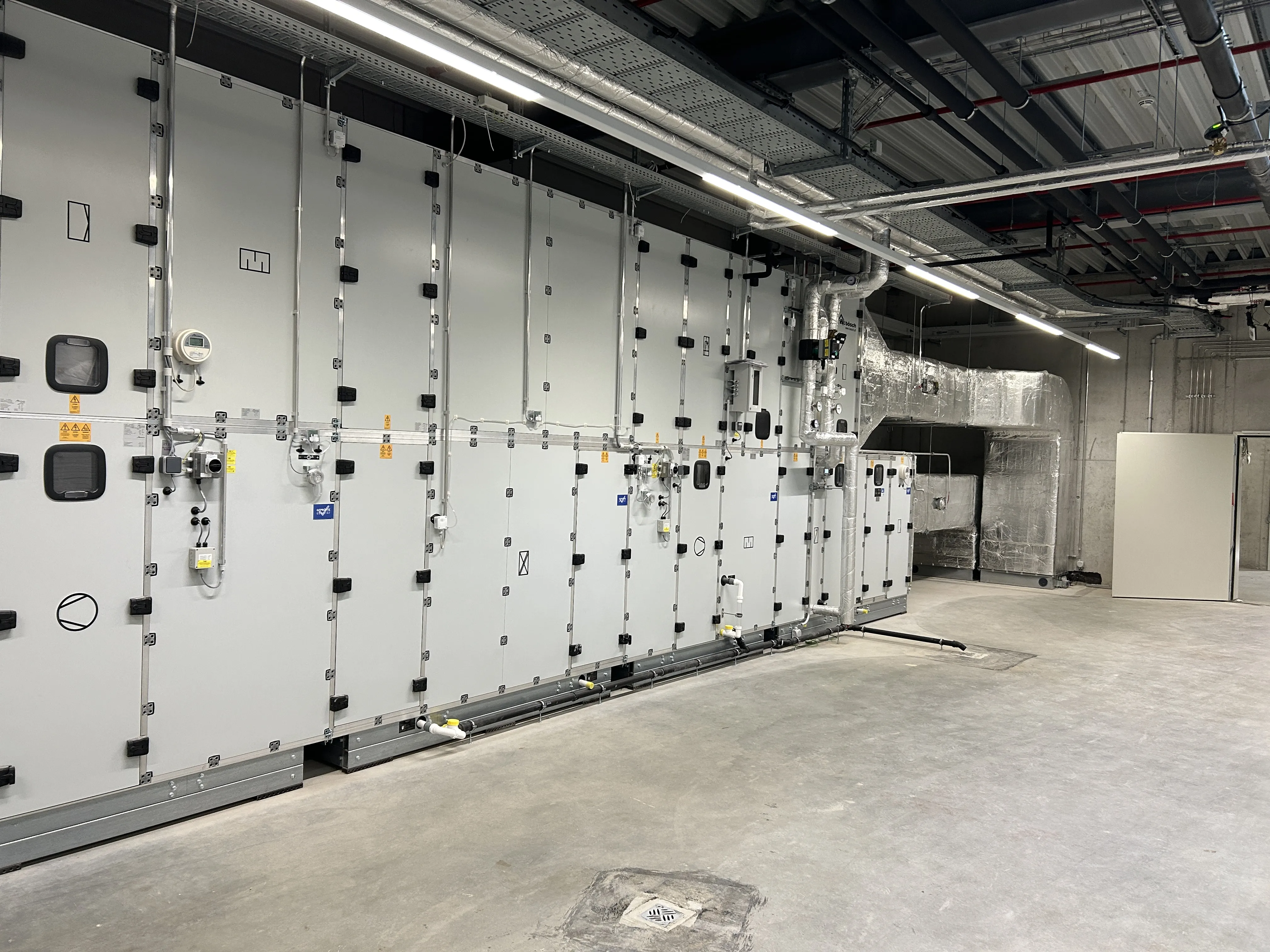 Ein geräumiger Technikraum mit einer großflächigen Lüftungszentrale, ausgestattet mit modularen Geräteeinheiten und zahlreichen Steuerungskomponenten.