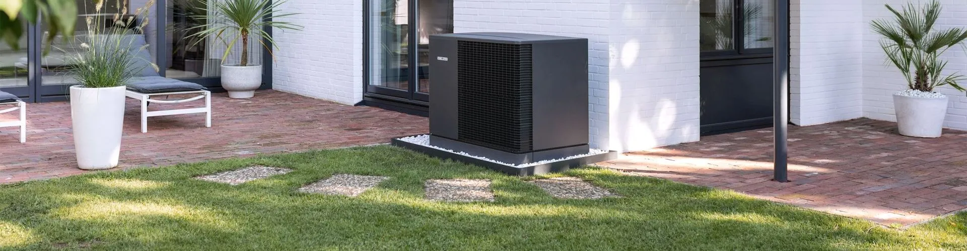 Eine grau-schwarze Wärmepumpe von Stiebel Eltron steht auf einem weißen Eckhaus im Garten.