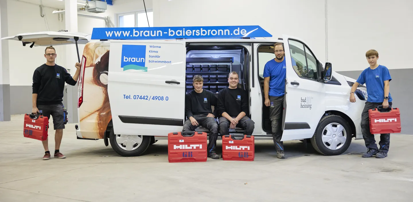 Eine Gruppe von Mitarbeitenden der Gottfried Braun GmbH posiert mit Werkzeugkoffern vor einem Servicefahrzeug in einer Werkhalle.