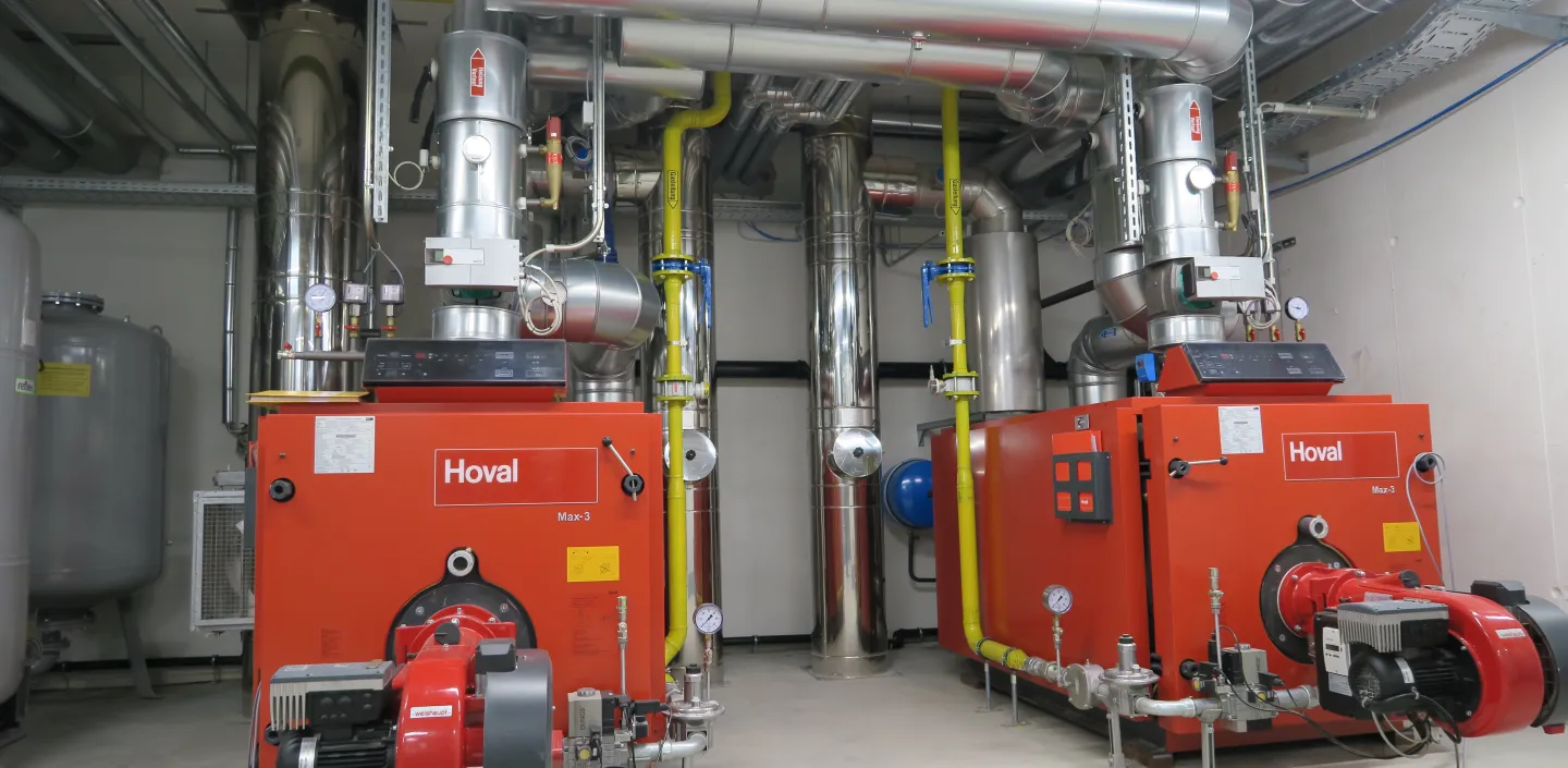 Zwei große, rote Heizkessel der Marke Hoval stehen nebeneinander in einem modernen Technikraum.