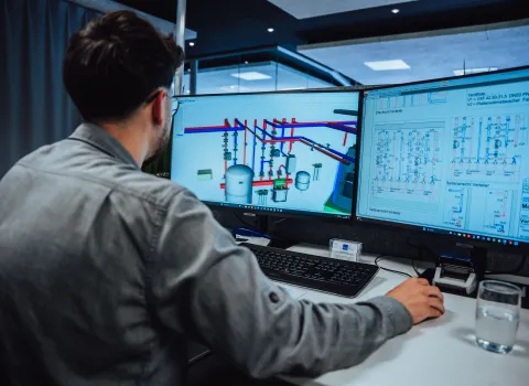 Mitarbeiter arbeitet am Computer mit CAD-Software und technischen Rohrleitungsplänen auf zwei Monitoren.