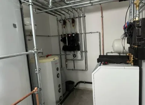 Technikraum mit moderner Heizungsanlage, Pufferspeicher, Rohrleitungen und Verteilereinheit für Warmwasser und Heizsystem.