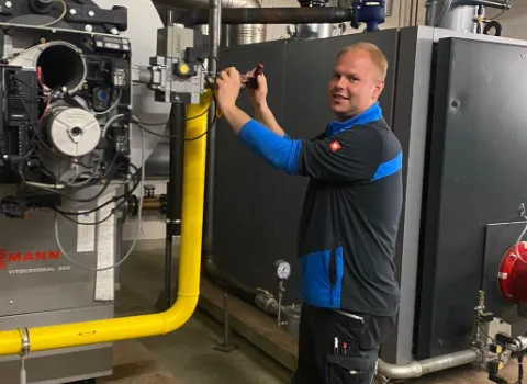 Servicetechniker arbeitet an einer großen Heizungsanlage in einem Technikraum und führt Wartungsarbeiten an den Rohrleitungen durch.