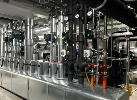 Technikraum mit komplexer Heizungs- und Gebäudetechnik: Rohrleitungen, Pumpen, Ventile und Messgeräte in industrieller Ausführung.