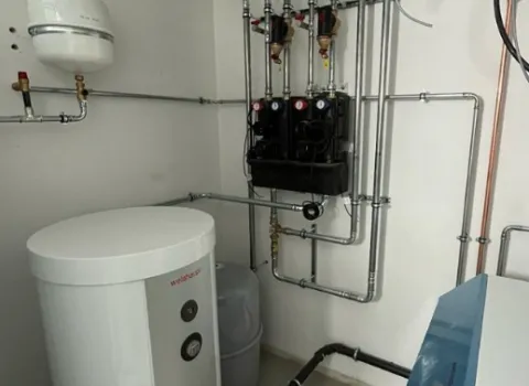 Moderne Heizungs- und Warmwasseranlage mit Pufferspeicher, Rohrleitungen und Verteilereinheit in einem Technikraum.