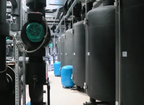 Technikraum mit großen schwarzen Pufferspeichern, Rohrleitungen und Pumpenanlagen zur Wärme- und Energieversorgung.