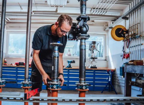 Monteur richtet in der Werkstatt ein Rohrsystem mit Flanschen aus, im Hintergrund sind Werkzeuge und Maschinen sichtbar.