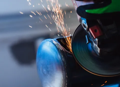 Nahaufnahme eines Handwerkers, der mit einem Winkelschleifer Metall bearbeitet – Funkenflug während der Arbeit.