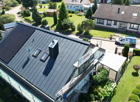 Luftaufnahme eines Hauses mit frisch saniertem, dunkel gedecktem Dach und einer großen Photovoltaikanlage auf der linken Dachfläche.