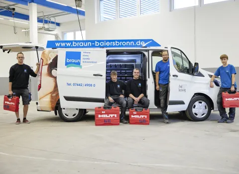 Eine Gruppe von Mitarbeitenden der Gottfried Braun GmbH posiert mit Werkzeugkoffern vor einem Servicefahrzeug in einer Werkhalle.