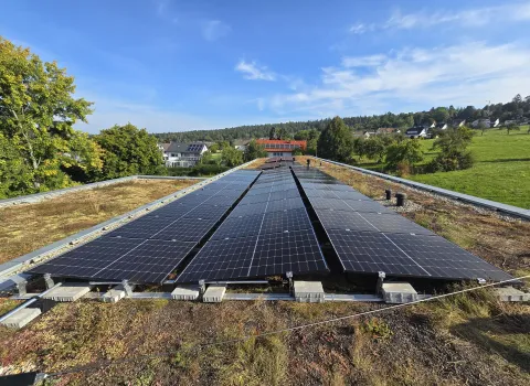 Flachdach-Solaranlage auf begrüntem Dach mit Blick auf eine ländliche Ortschaft und umgebende Bäume.