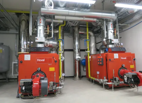 Zwei große, rote Heizkessel der Marke Hoval stehen nebeneinander in einem modernen Technikraum.