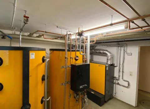 Ein moderner Heizungsraum mit einem zentralen Pelletheizkessel der Marke ETA und mehreren großen Pufferspeichern in leuchtendem Gelb.