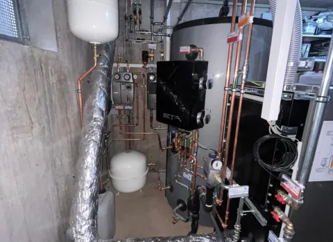 Ein komplexer Heizungsraum mit einer modernen ETA-Pelletanlage, einem großen Wärmespeicher und zahlreichen Kupfer- und Isolierleitungen.