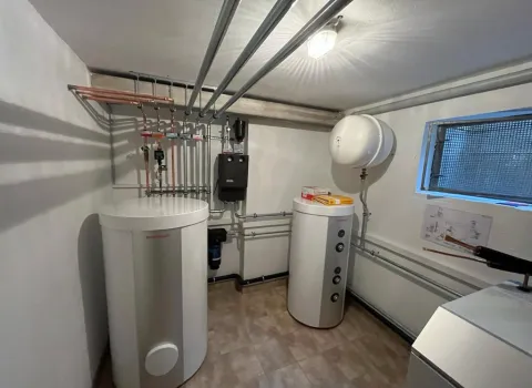 Ein sauber installierter Heizungsraum mit moderner Wärmepumpentechnik zeigt zwei weiße Speichereinheiten und eine ordentliche Rohrinstallation an Wand und Decke.
