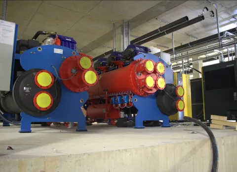 Eine industrielle Kältemaschine in einem Technikraum zeigt ein komplexes System aus großen Rohrleitungen, Kühlaggregaten und Steuerungseinheiten.