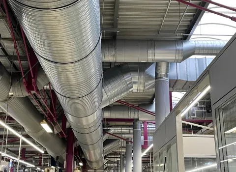 Groß dimensionierte Lüftungsrohre verlaufen unter der Hallendecke eines modernen Industriegebäudes.