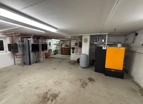 In einem großzügigen Heizraum ist rechts eine gelb-schwarze Pelletheizung der Marke ETA installiert, daneben ein graues Ausdehnungsgefäß.
