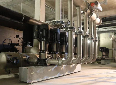 Das Bild zeigt eine moderne Pumpenanlage mit mehreren vertikal montierten Edelstahlpumpen der Grundfos-CR-Serie.