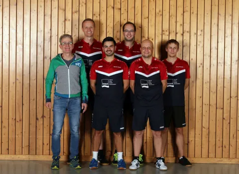 Gottfried Braun, Geschaeftsfuehrer der Gottfried Braun GmbH, steht mit sechs Spielern des Tischtennisvereins SG Baiersbronn-Klosterreichenbach vor einer Holzwand in der Turnhalle und lächelt in die Kamera.