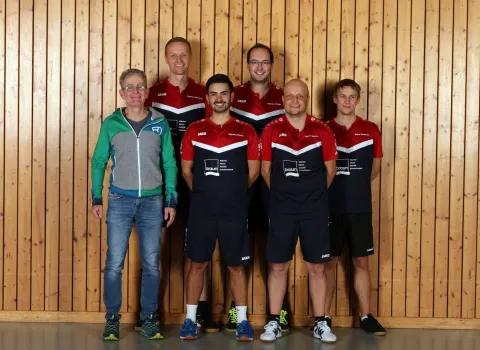 Gottfried Braun, Geschaeftsfuehrer der Gottfried Braun GmbH, steht mit sechs Spielern des Tischtennisvereins SG Baiersbronn-Klosterreichenbach vor einer Holzwand in der Turnhalle und lächelt in die Kamera.