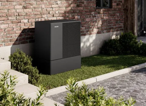 Eine schwarze Waermepumpe der WPL-A-Serie von Stiebel Eltron steht auf einer Rasenflaeche vor einem Altbau.