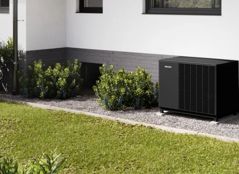 Eine Wärmepumpe von Stiebel Eltron steht im Garten auf einem schmalen Kiesbettstreifen vor dem Einfamilienhaus.