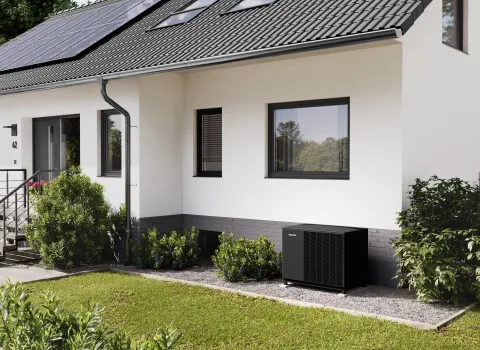 Eine schwarze Waermepumpenaußeneinheit von Stiebel-Eltron steht auf einem Kiesbett vor einem Einfamilienhaus.