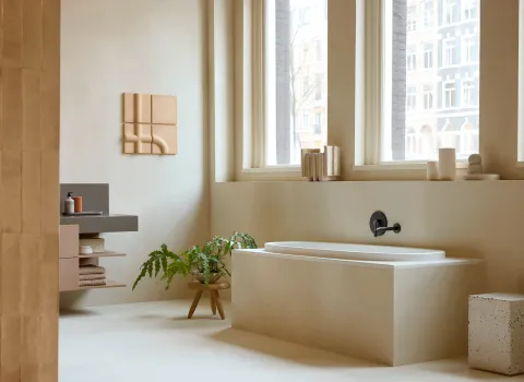 Moderne Duravit-Badewanne aus der Balcoon-Kollektion in minimalistischem Badezimmer mit warmen Naturtönen, Pflanzen und großem Fenster.