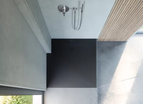 Moderne Dusche mit schwarzem Boden und minimalistischem Design in einem lichtdurchfluteten Badezimmer.