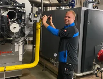 Servicetechniker arbeitet an einer großen Heizungsanlage in einem Technikraum und führt Wartungsarbeiten an den Rohrleitungen durch.