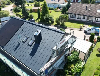 Luftaufnahme eines Hauses mit frisch saniertem, dunkel gedecktem Dach und einer großen Photovoltaikanlage auf der linken Dachfläche.
