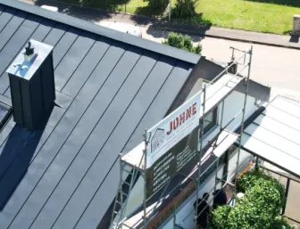 Luftaufnahme eines Wohngebäudes mit neuem, dunkel gedecktem Schrägdach und großflächiger Photovoltaikanlage auf der linken Dachseite.