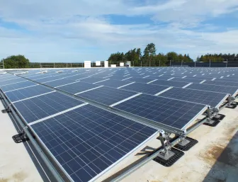 Große Photovoltaikanlage auf einem Flachdach unter blauem Himmel, aufgenommen in einer weitläufigen Umgebung.