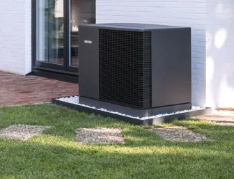 Eine grau-schwarze Wärmepumpe von Stiebel Eltron steht auf einem weißen Eckhaus im Garten.