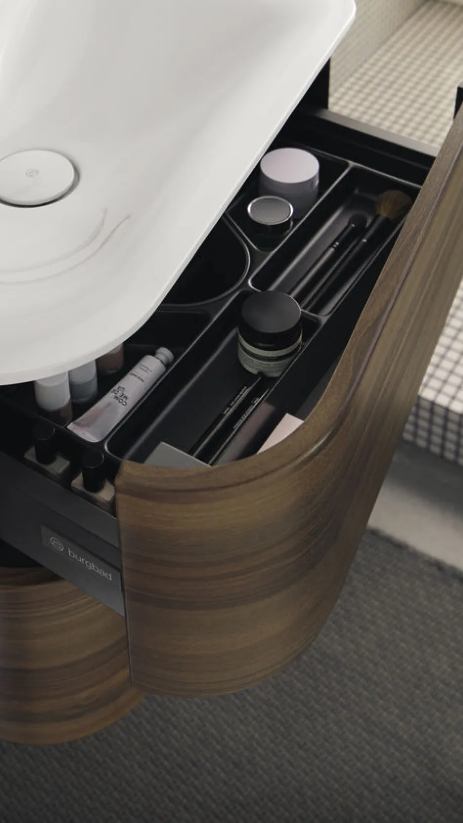 Detailaufnahme eines Burgbad Badu Badmöbels mit geöffneter Schublade, in der verschiedene Pflege- und Kosmetikartikel ordentlich sortiert sind.