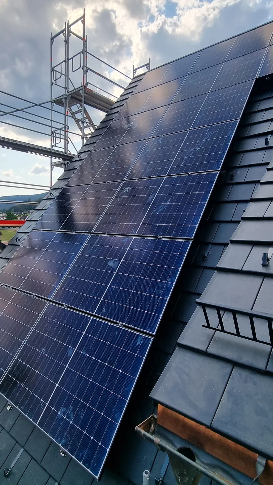 Schrägdach-Solaranlage auf dunklen Dachziegeln mit Gerüst im Hintergrund und bewölktem Himmel.