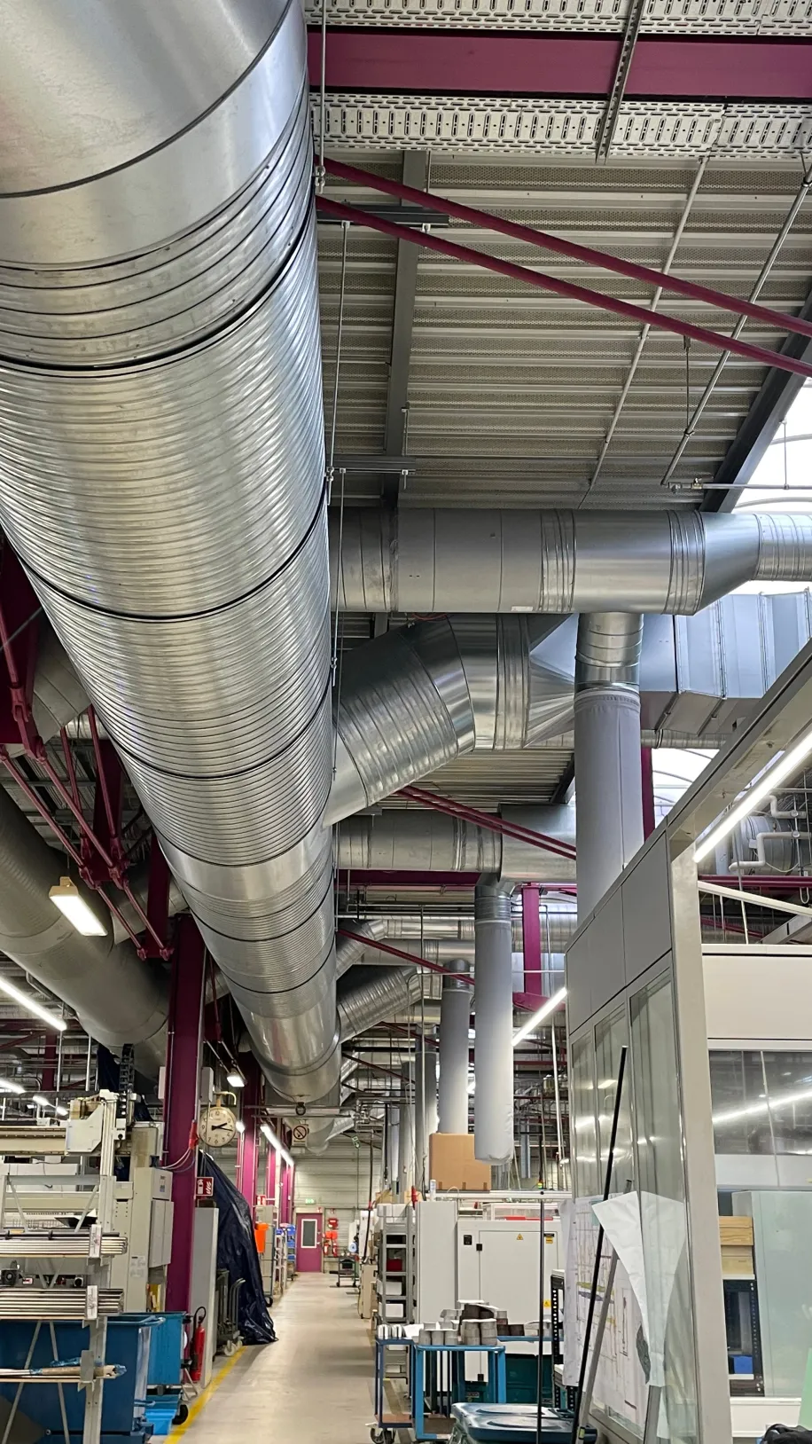 Groß dimensionierte Lüftungsrohre verlaufen unter der Hallendecke eines modernen Industriegebäudes.