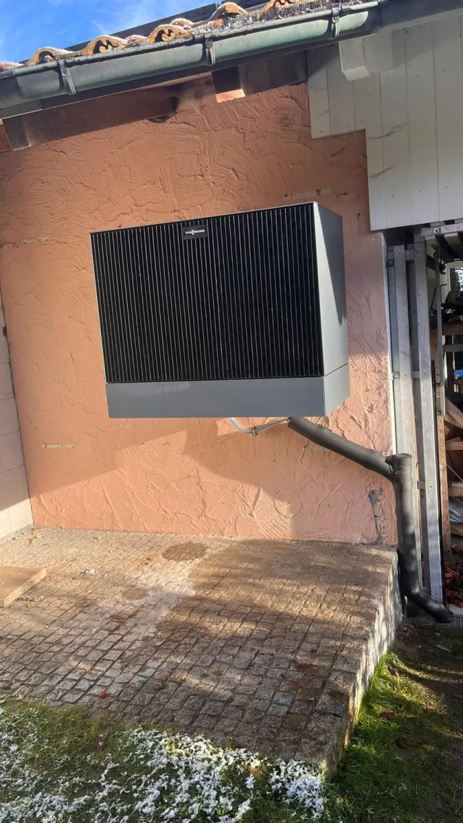 Eine Wärmepumpe der Marke Viessmann ist an der Außenwand eines älteren Hauses mit rosafarbener Putzfassade montiert.