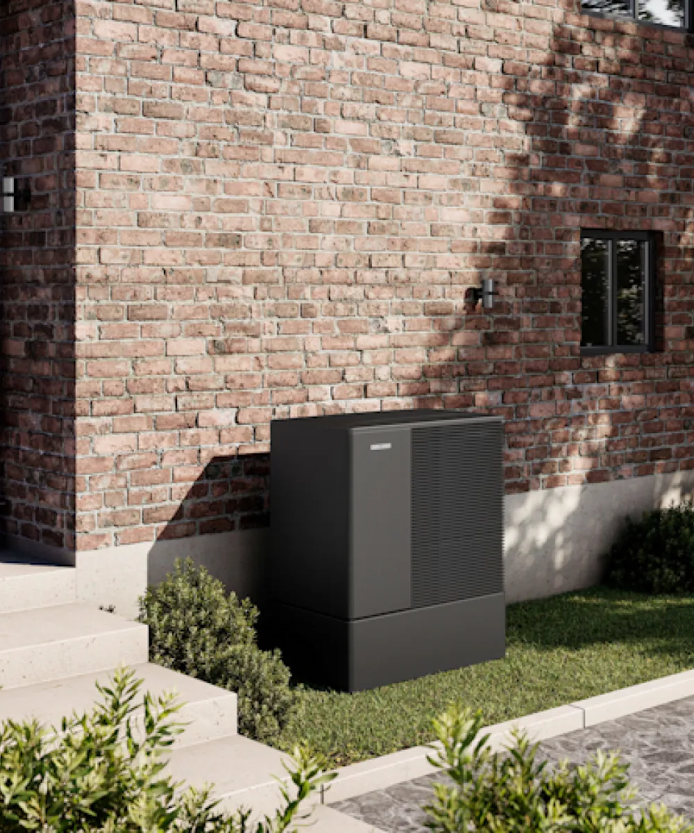 Eine schwarze Wärmepumpe von Stiebel Eltron steht vor einem Backsteinhaus.