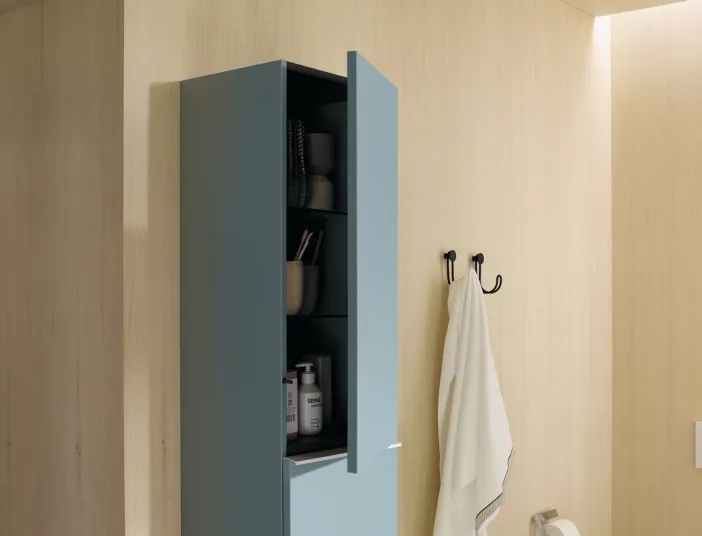 Ein geöffneter, hellblauer Hochschrank der Fiumo-Kollektion von burgbad zeigt dunkle Regale mit Pflegeprodukten und Badezimmerutensilien.