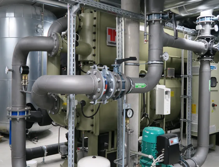 Technikraum mit industrieller Kälteanlage, großen Rohrleitungen, Umwälzpumpe und Wärmetauscher der Marke Thermax.