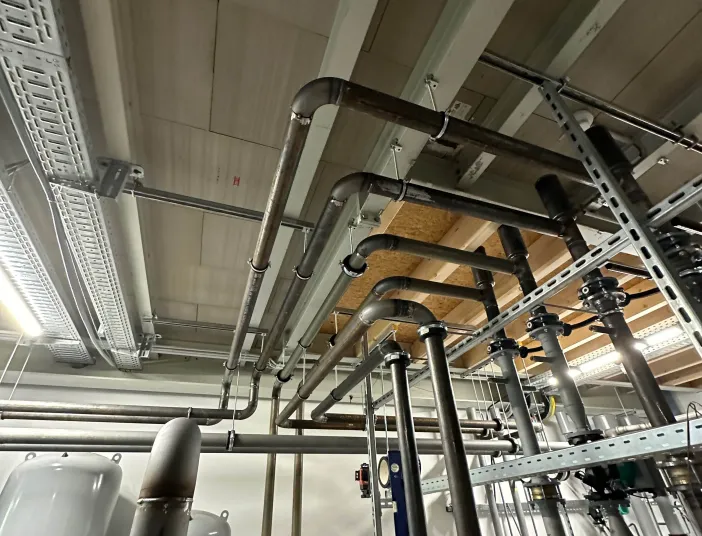 Verrohrung und technische Installation einer Kälteanlage in einem Maschinenraum, mit Druckbehältern, Ventilen und Leitungen unter der Decke.