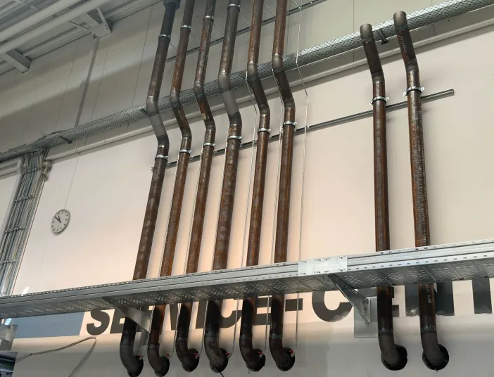 Vertikale Rohrleitungen einer industriellen Kälteanlage, sauber verlegt und mit Befestigungen an der Wand einer Werkshalle montiert.